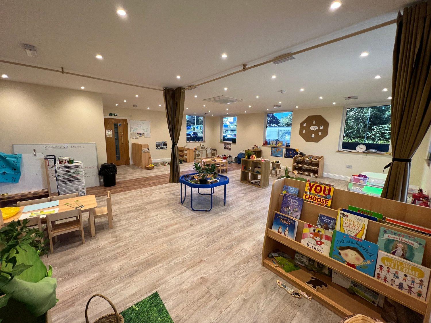 A preschool room with books, writing areas, tables, and windows onto trees