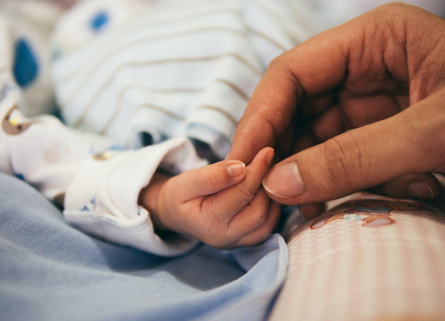A baby's hand held gently by an adult