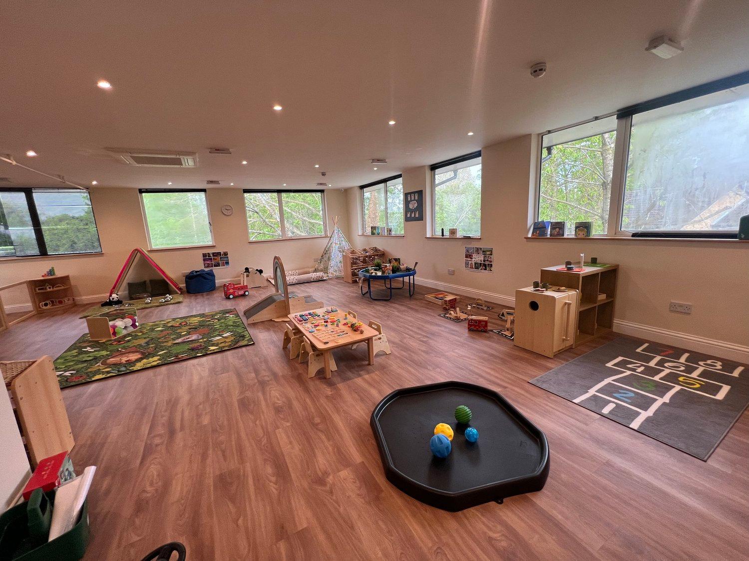 A bright toddler room with role-play spaces, a slide, and accessible resources
